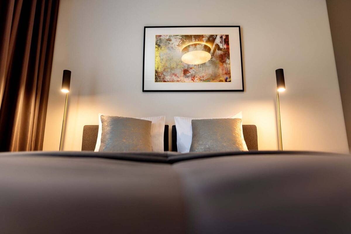 Une chambre d’hôtel avec un lit, deux lampes de chevet et un tableau abstrait encadré accroché au mur.