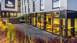 Een modern gebouw met een Hessner logo, grote glasramen en een terras.