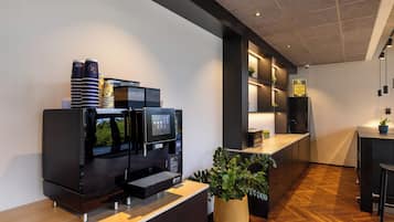 Un área de recepción moderna con una máquina de café, un televisor de pantalla plana y una planta en maceta.