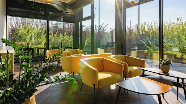 Een moderne binnenruimte met grote ramen, gele stoelen en een houten tafel.