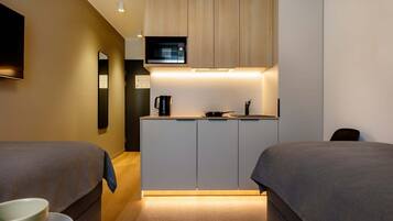 A modern hotel room with a kitchenette, two beds, a flat-screen TV, and a small mirror.
