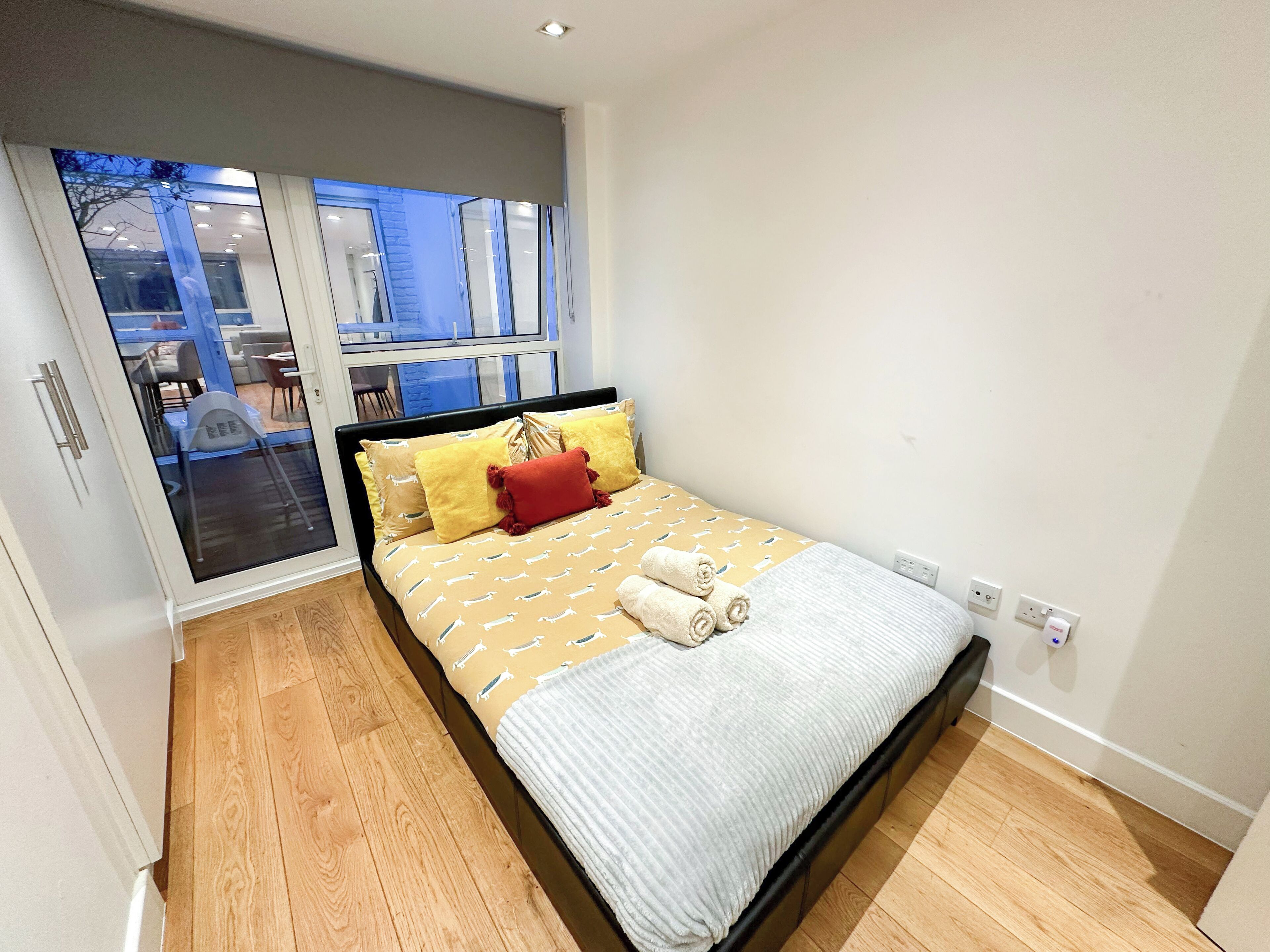 A modern bedroom with a large bed, a sliding glass door leading to an outdoor area, and a view of the cityscape.