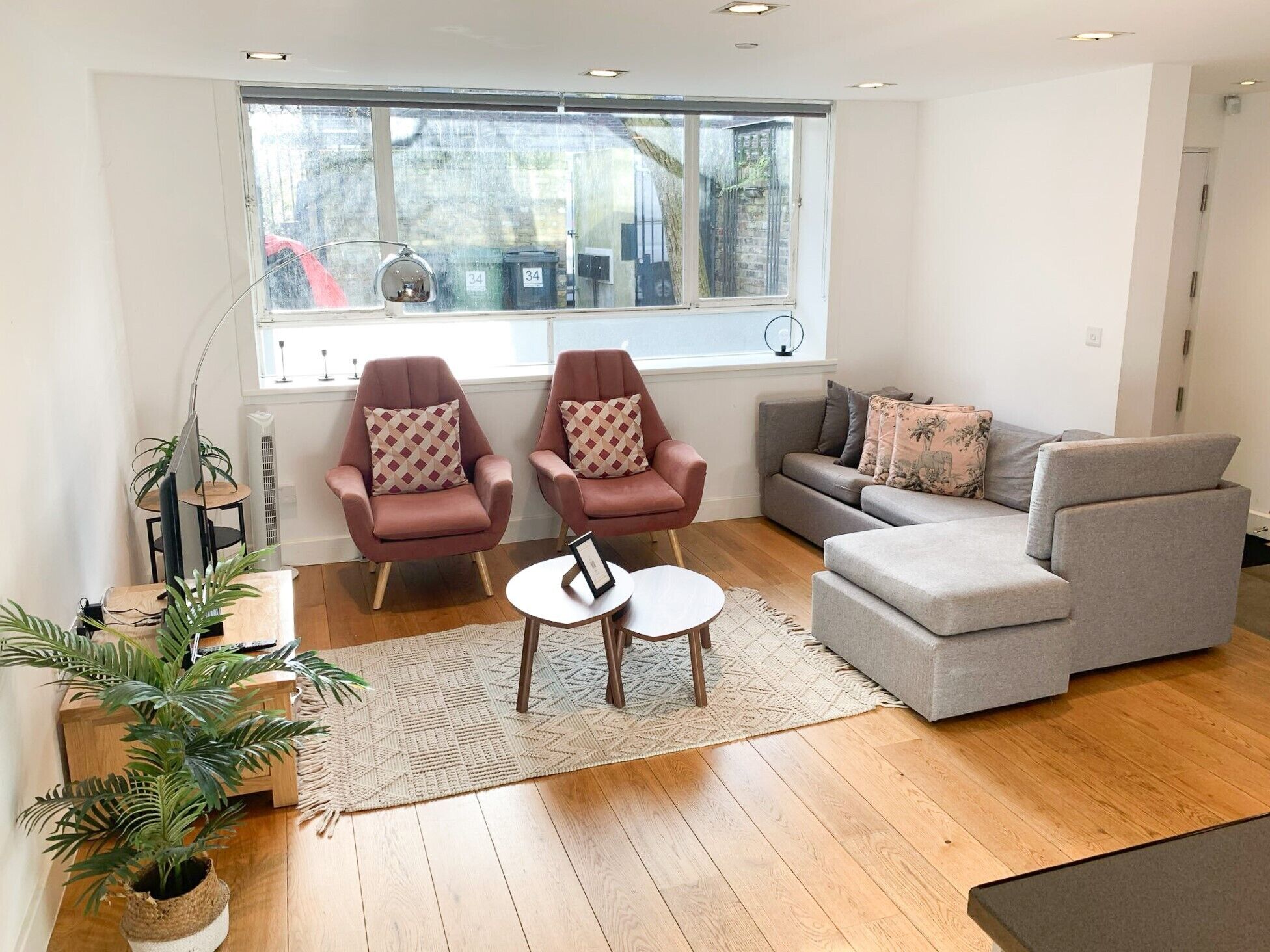 Un salon moderne avec deux fauteuils, un canapé gris, une petite table basse et une grande fenêtre donnant sur la rue.