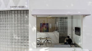 A modern building with a glass entrance, a bicycle parked outside, and a person sitting inside. - Meow Hero Youth Hostel (Shanghai)