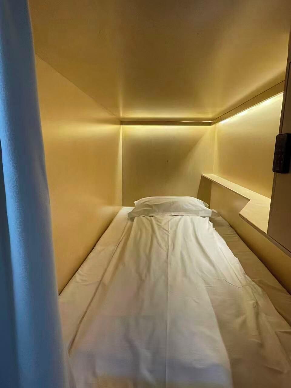 A single bed in a room with a plain wall and a small bedside table.