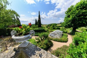 Un jardín con una urna decorativa, un invernadero y setos perfectamente recortados.
