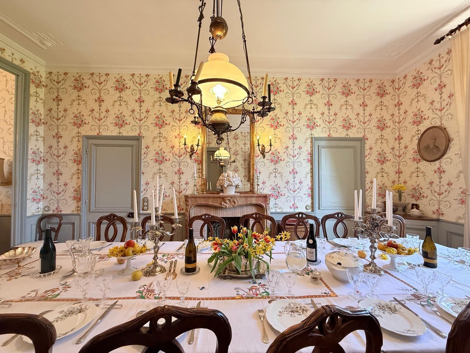 Comedor con candelabro, papel tapiz floral y una mesa dispuesta para una comida.