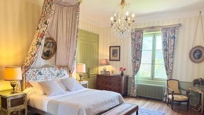 A classic bedroom with a four-poster bed, a chandelier, a wooden bench, a dresser, and a chair. - Domaine de Montclair (Pommiers)