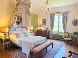 Un dormitorio clásico con cama con dosel, candelabro, banco de madera, cómoda y silla.