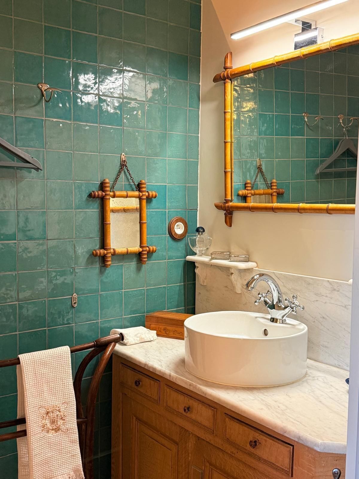A bathroom with a white sink, wooden towel rack, and a mirror with a bamboo frame.