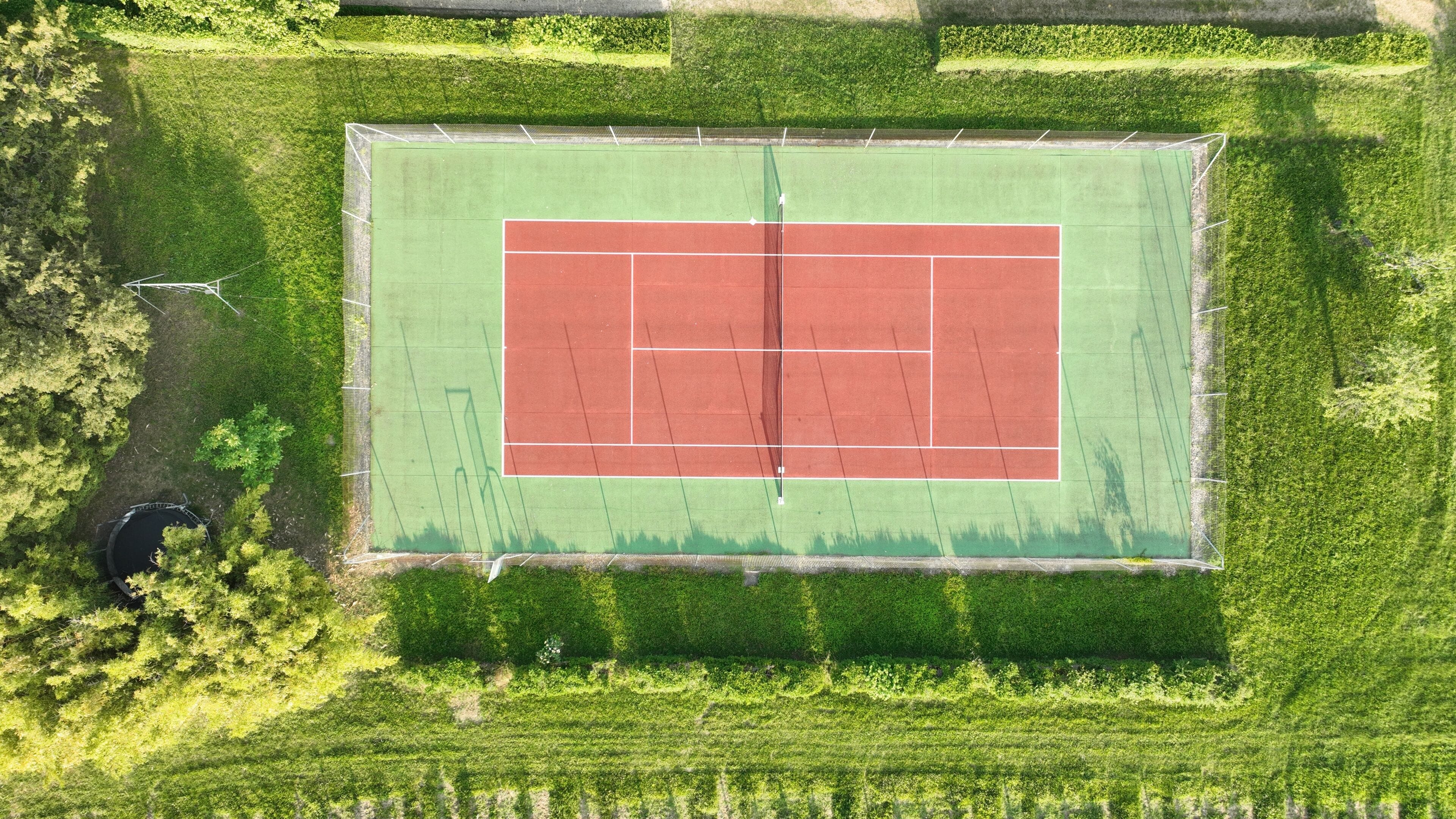 Vista aérea de una cancha de tenis rodeada de césped verde y árboles.