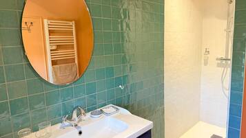 Un baño con lavamanos, espejo, toallero y ducha.