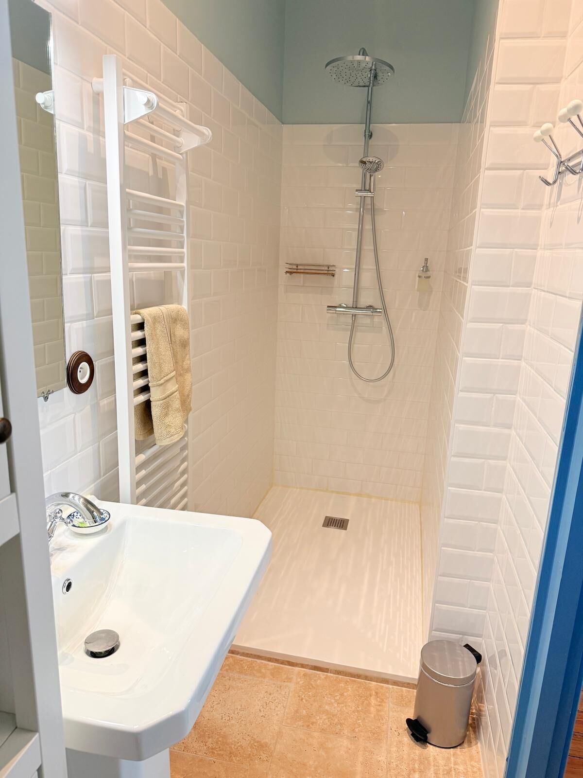 A bathroom with a shower, sink, towel rack, and a trash bin.