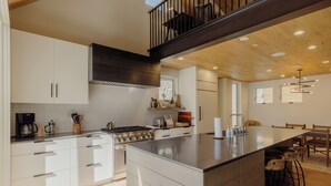 Une cuisine moderne avec des meubles blancs, un grand îlot central et un coin repas doté de chaises en bois.