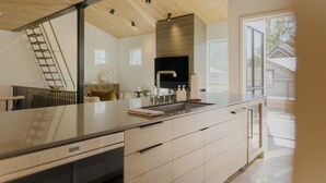 Une cuisine moderne dotée d’un grand îlot central, d’appareils électroménagers en acier inoxydable et offrant une vue sur l’extérieur.