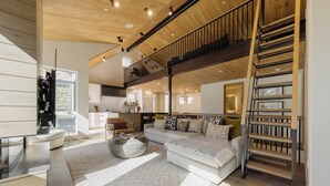 Un vaste espace de vie doté d’un haut plafond, d’un escalier et d’une cuisine moderne en arrière-plan.