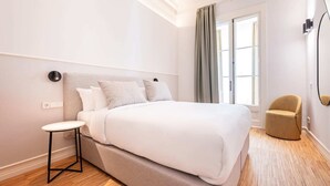 Une chambre d’hôtel moderne avec un grand lit, une petite table ronde, une chaise et une grande fenêtre avec des rideaux.