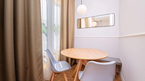 Une pièce moderne avec une table ronde en bois, deux chaises grises, un banc, un luminaire suspendu et un miroir au mur.