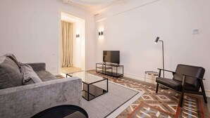 A modern living room with a sofa, a coffee table, a TV on a stand, a chair, and a patterned rug. - Sweett | Gran Via 204 (Barcelona)