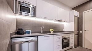 A modern kitchen with stainless steel appliances, white cabinetry, and a built-in dishwasher. - Sweett | Gran Via 302 (Barcelona)