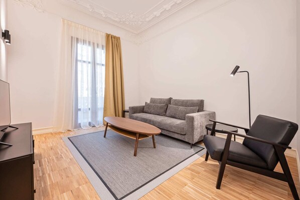 Een moderne woonkamer met een grijze bank, een houten salontafel, een zwarte leren fauteuil en een vloerlamp.