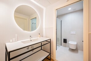 Een moderne badkamer met een witte wastafel, een ronde spiegel en een toilet.