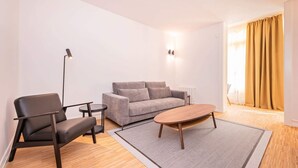 A modern living room with a grey sofa, a black chair, a wooden coffee table, and a floor lamp. - Sweett | Gran Via 104 (Barcelona)