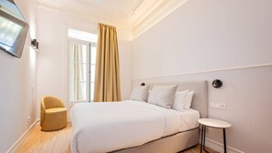 A modern bedroom with a large bed, a small round table, and a chair. - Sweett | Gran Via 104 (Barcelona)