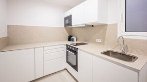 A modern kitchen with white cabinets, a built-in oven, a microwave, and a stainless steel sink. - Sweett | Gran Via 104 (Barcelona)