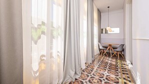 A corridor with a patterned floor, a dining area with a table and chairs, and sheer curtains allowing natural light. - Sweett | Gran Via 202 (Barcelona)