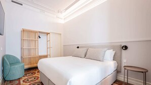 A hotel room with a bed, a chair, a wardrobe, and a small table. - Sweett | Gran Via 202 (Barcelona)