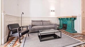 A living room with a grey sofa, a black leather chair, a glass coffee table, a patterned rug, and a green fireplace. - Sweett | Gran Via 202 (Barcelona)
