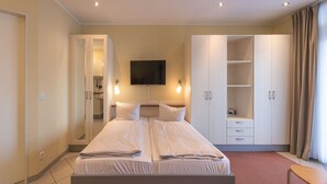 A double bed with a flat-screen TV above it, a wardrobe with multiple doors, and a bathroom visible through an open door. - Ferienwohnung im Aparthotel Seepanorama (Mirow)