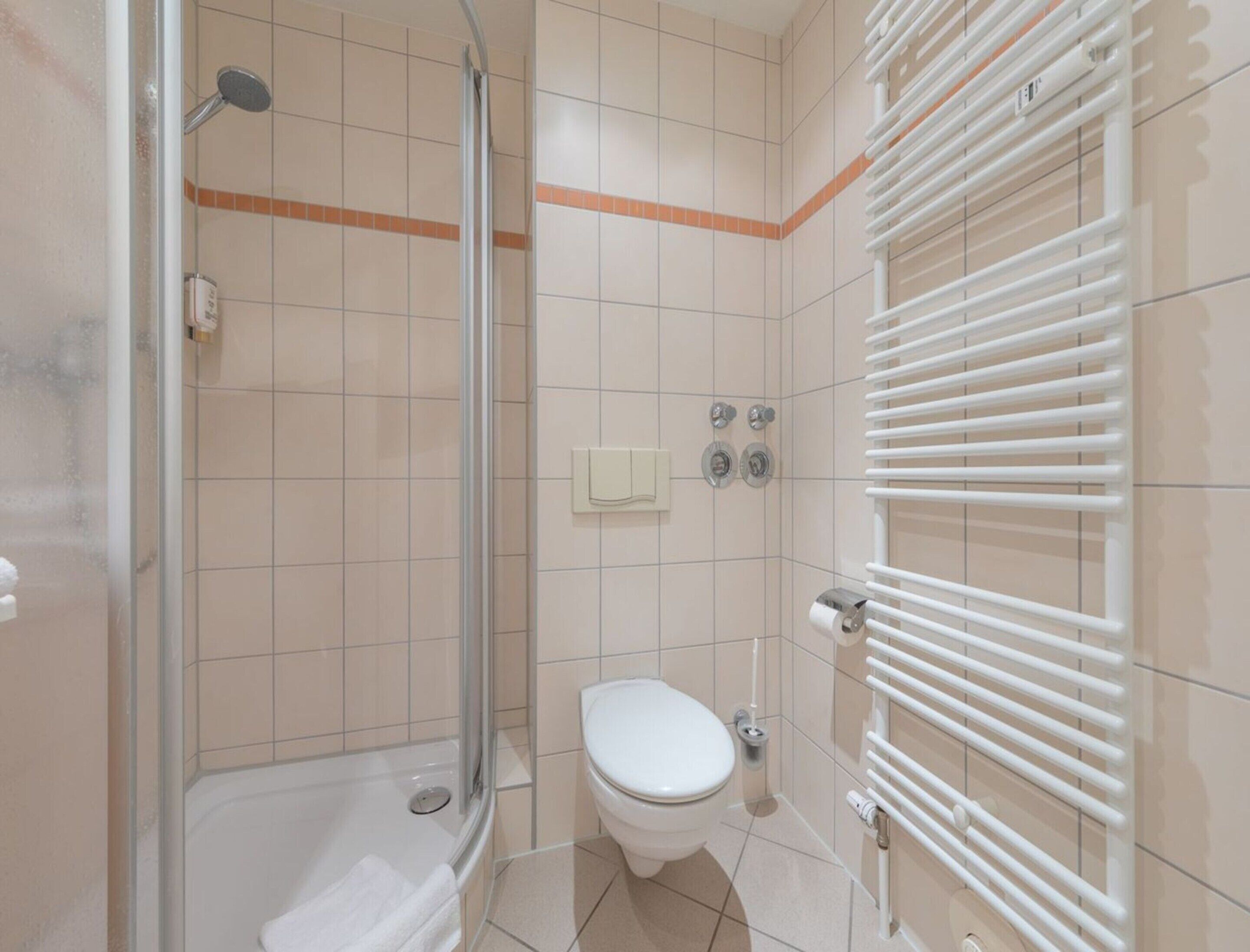 A bathroom with a glass-enclosed shower, a toilet, and a white radiator.