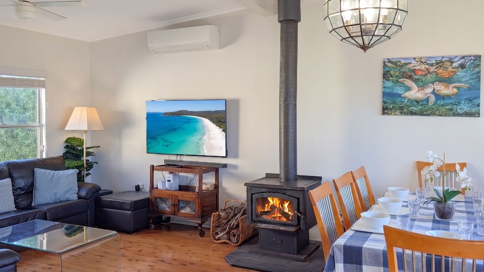 A living room with a TV, a fireplace, a dining table set for two, and a painting on the wall.