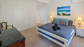 Une chambre à coucher comprenant un lit, des tables de chevet, un bureau, une chaise, un tableau et une armoire.