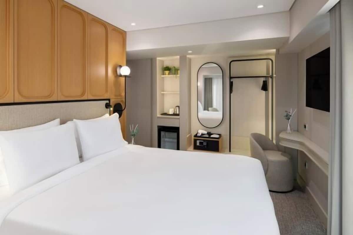 Quarto de hotel com cama grande, mesa de cabeceira, espelho, televisão e guarda-roupa.