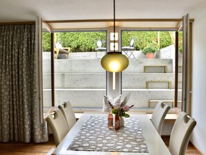 Un coin repas avec une table dressée pour quatre personnes, un vase rempli de fleurs et un luminaire suspendu.
