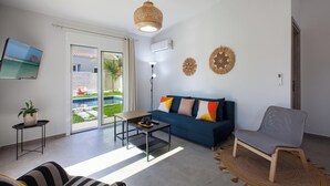 Un salon moderne avec un canapé, un fauteuil, une table basse et un téléviseur fixé au mur.