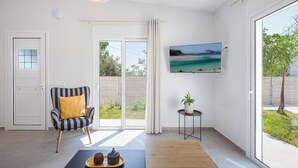 Un salon moderne doté d’une grande porte-fenêtre coulissante donnant sur un balcon, d’un fauteuil à rayures avec un coussin jaune, d’un téléviseur à écran plat fixé au mur et d’une petite table d’appoint sur laquelle est posée une plante.