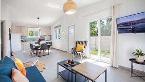 Un salon moderne avec un canapé, une table basse et un téléviseur. On y trouve également un coin repas avec des chaises et une table, ainsi qu’une cuisine à l’arrière-plan.
