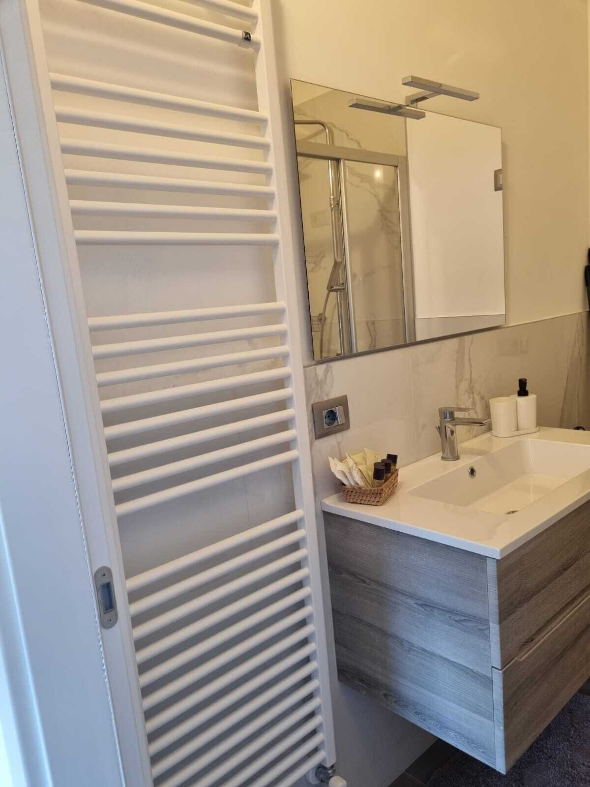 Ein modernes Badezimmer mit einem weißen Handtuchhalter, einem Spiegel, einem Waschbecken mit Marmorplatte und einer Holzkommode.