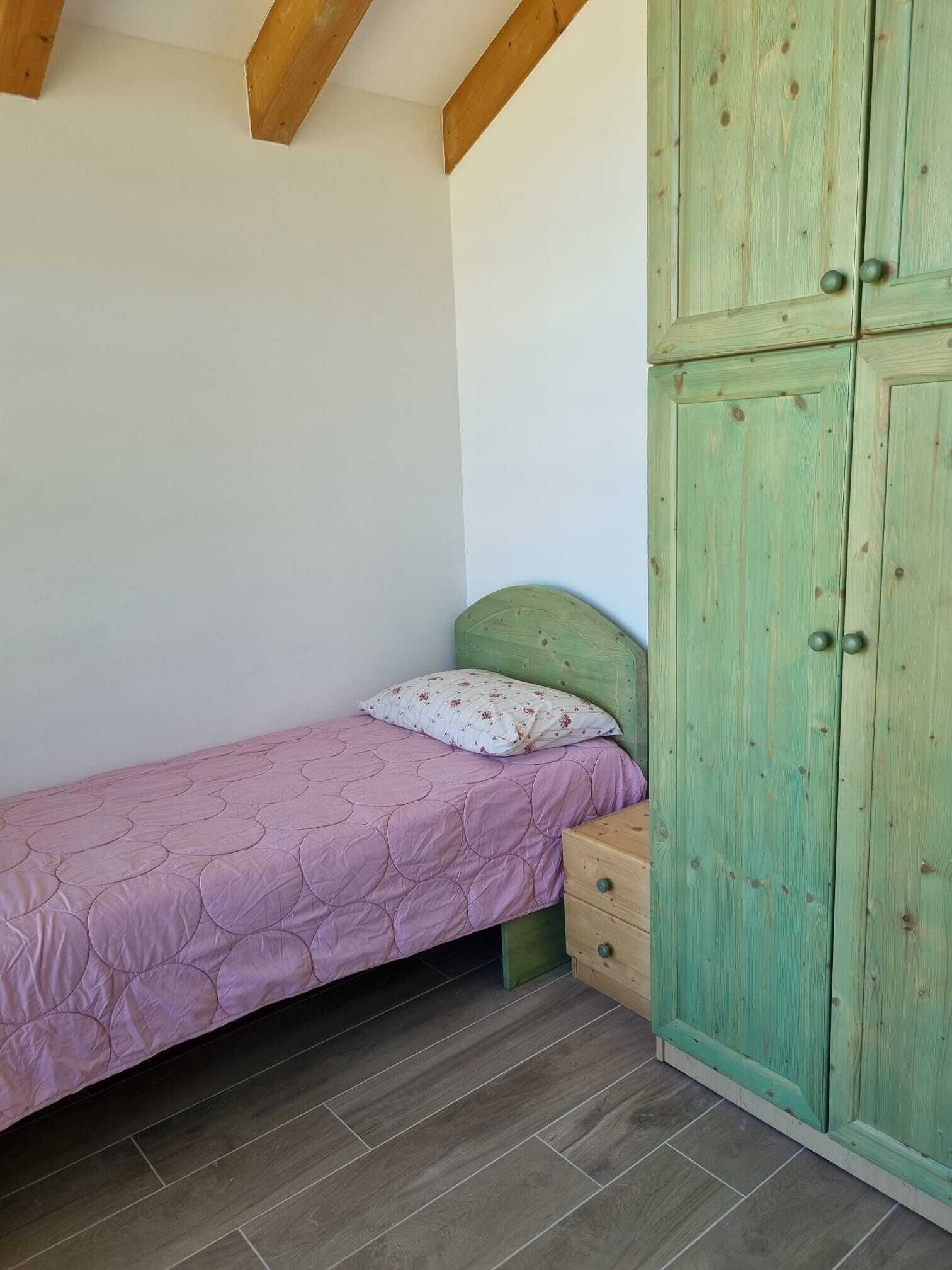 A small bedroom with a single bed, a green wardrobe, and a wooden ceiling.