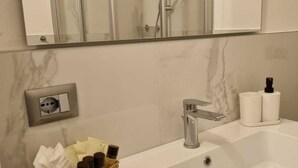 A bathroom with a white sink, a mirror above it, a shower enclosure, and toiletries on the sink.