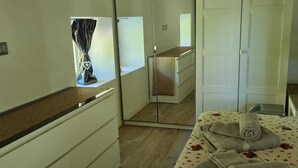 A bedroom with a wooden ceiling, a bed with a floral bedspread, a dresser, a mirror, and a wardrobe.