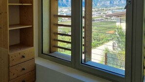 A room with a large window, wooden shelving, and a view of mountains and a town.