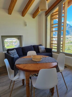 A cozy room with a dark blue sofa, white chairs, a wooden table, and a view of a mountainous landscape through large windows. - FARM KREUZBERG ATTIC WITH TWO ROOMS MOUNTAIN VIEW (Trentino-Alto Adige)
