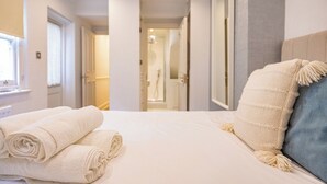 A hotel room with a neatly made bed, a window with curtains, and a door leading to a bathroom. - Charming 3-Bed Haven in Little Venice with a Private Outdoor Oasis (London)