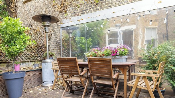 An outdoor patio with a wooden table and chairs, surrounded by potted plants and a brick wall. - Charming 3-Bed Haven in Little Venice with a Private Outdoor Oasis (London)