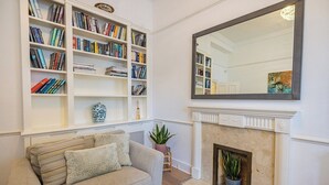 A living room with a fireplace, a sofa, a bookshelf, and a mirror. - Charming 3-Bed Haven in Little Venice with a Private Outdoor Oasis (London)